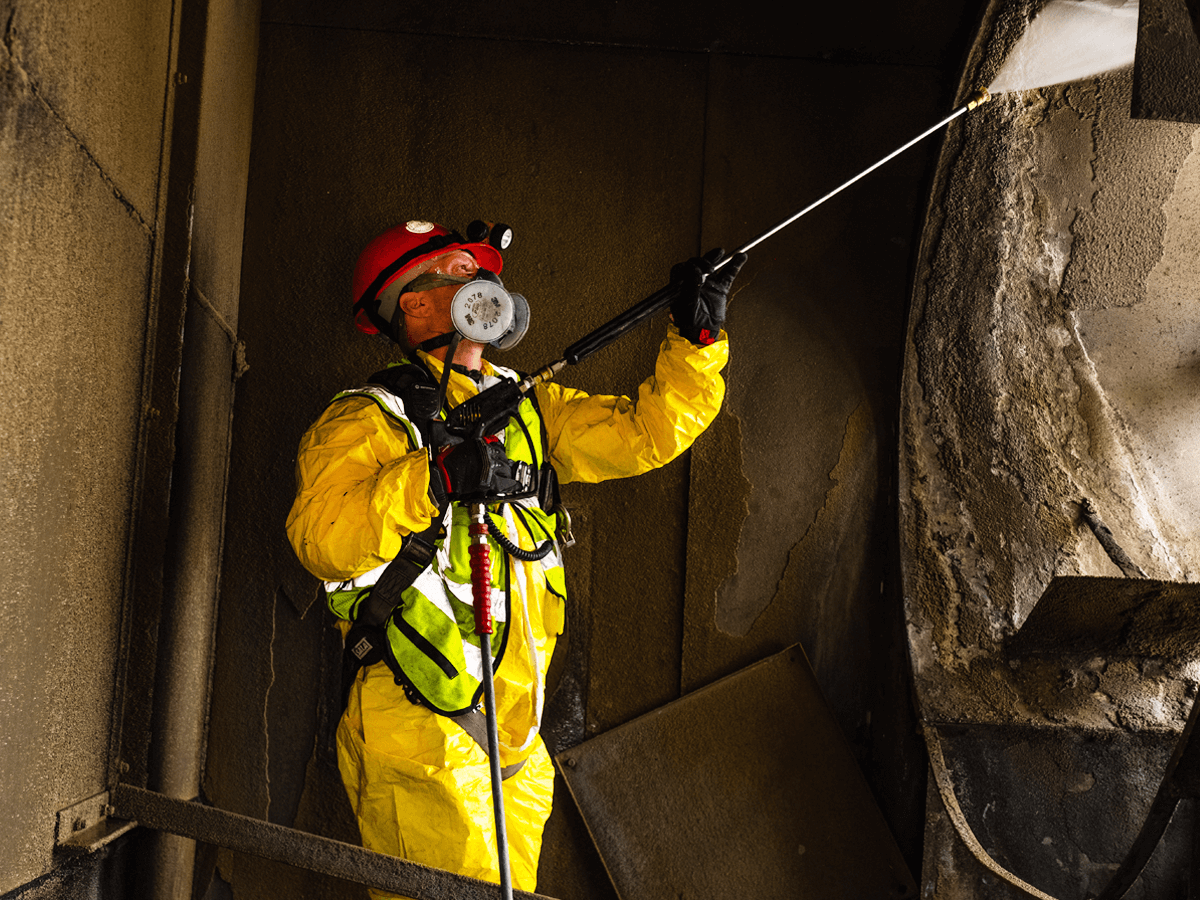 Media blasting worker in full PPE: face shield, gloves, protective coveralls
